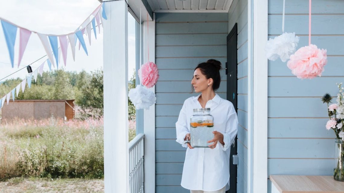 Woman holding lemonade jar at decorated house entrance for a summer party.